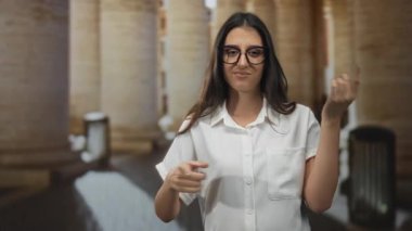 Genç İspanyol kadın, eski şehir sokağında elini ve avucunu taştan sütunlarla işaret ediyor..