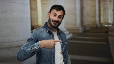 Sakallı bir adam Roma 'daki antik sütunların arasında jest yapmaz, tarihi eski şehir ortamında dinamik bir anı yakalar kot ceket ve kendine güvenen bir ifadeyle.