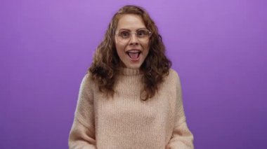 Mor arka planda gülümseyen gözlüklü ve süveterli bir kadın stüdyo ortamında neşe ve sıcaklığın neşeli bir ifadesi sergiliyor..
