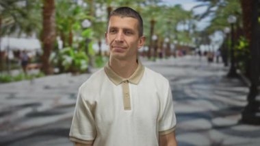 Man outdoors on a vibrant street with palm trees and a casual atmosphere, showcasing a thoughtful expression in a relaxed setting during the day.
