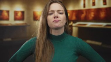 Modern müzedeki sanat eserlerini işaret eden ve kulağına dokunan kadın, merak yansıması.