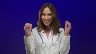 Steteskop takan genç İspanyol kadın doktor canlı mavi bir arka plana, sağlık alanında profesyonelliği ve pozitifliği somutlaştıran güvenle gülümsüyor..