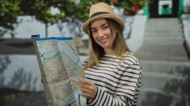 Canlı bir caddeyi keşfeden genç bir kadın, neşeli bir ifadeyle bir harita tutuyor, açık hava macerasını kucaklıyor ve canlı bir şehir ortamında seyahat merakı içinde..