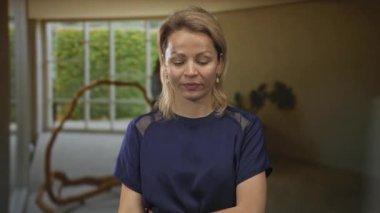 Genç sarışın kadın, stüdyoda yüzün yanında bej renkli duvarda doğal ışığı olan büyük pencerenin yanında altın bir waffle tutuyor..