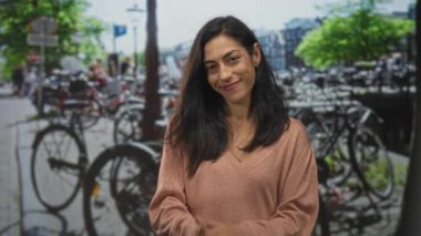 Park halindeki bisikletlerin yanında el çırpan, gülümseyen ve kameraya bakan bir kadın..
