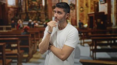 Eli çenesinde olan bir adam kilise binasında beyaz gömlek ve bilezik giyen düşünceli bir duruş, dik dik baktı; düşüncelere daldı.