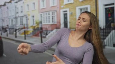 Uzun saçlı genç bir kadın renkli bir şehir caddesinde halat çekme hareketini eğlenceli bir şekilde taklit ediyor.