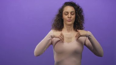 Genç İspanyol kadın göğsünü işaret ediyor ve mor stüdyoda el ele tutuşuyor..