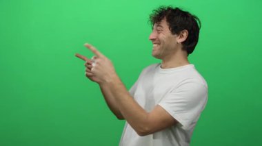 Beyaz gömlekli İspanyol adam gülümsüyor ve canlı yeşil bir arkaplanı işaret ediyor.