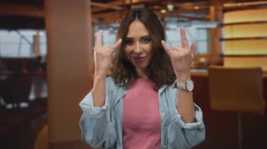 Genç bir kadın otel ortamında sıcak, çevresel aydınlatma ve modern dekorun altını çizerek rahat bir şekilde gülümsüyor..