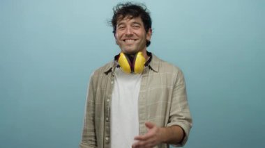 Sarı ses çıkaran İspanyol bir adam kulaklık takıyor. Mavi bir arka plana uzanan bir el ile gülümseyerek dostça ya da misafirperver bir jest öneriyor..
