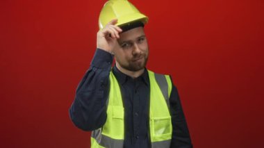 Kırmızı stüdyoda yüksek görünürlüklü yelek giyerken sarı başlık takan bir adam..