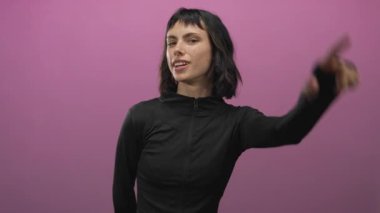 Pembe stüdyo ortamında alnında ezik işareti oluşturan kadının yüzü ve dili buruşmuş; şakacı meydan okuma.