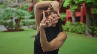 Ormandaki yemyeşil yapraklar ve ağaçlara karşı parmaklarıyla dış mekan sahnesini çerçeveleyen kadın, vizyon ilhamı.