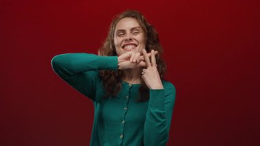 Yeşil kazaklı gülümseyen kadın kırmızı arka planda hashtag hareketi yaparak modern iletişim ve sosyal medya etkileşimini aktarıyor.