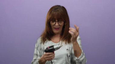 Üst düzey İspanyol kadın, izole edilmiş mor arka plan, merak ve odak gösteren kablosuz matkabı inceliyor..