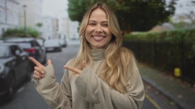 Şehir caddesinde bir kadını işaret eden uzun sarı saçlı, bej renkli bir kazak giyen bir kadın..