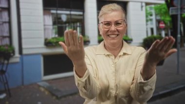 Bir bina ve pencere önünde açık bir sokakta açık avuçlar ile gülümseyen kadın; nezaket sevinç karşılama.