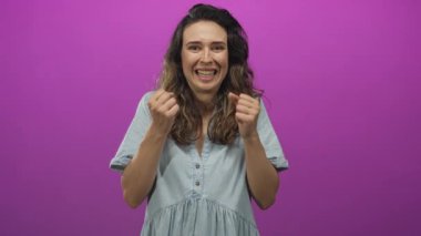İspanyol kadın sıkılmış yumruklarını kaldırır ve canlı mor bir stüdyo sahnesinde avuçlarını açar; heyecan zaferi kutlaması.