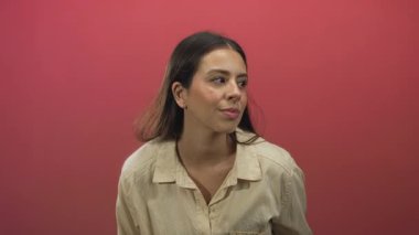 Yanlara bakan genç esmer kadın pembe stüdyoda yüzünü ve yakasını gösterir; dingin yansıma anı.