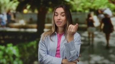 Güneşli bir park ortamında, kendine güvenen bir ifadeyle gözlerini gösteren bir kadın. Etrafı yemyeşil ve bulanık insanlarla çevrili. Odaklanma ve öz farkındalığı ön plana çıkaran bir kadın..