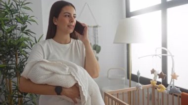 Genç esmer kadın bir binada ahşap bir beşiğin yanında bir örgü battaniye ve telefon ile kulağına tutarak; şefkat aile bakımı.