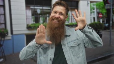 Geniş çerçeveli gülümseyen adam kent sokak binasına karşı elleri ile atış hareketi; yaratıcı mutluluk.