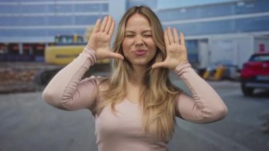 Kadın yüzünü makinelerin ve inşaat malzemelerinin önündeki inşaat sahasında elleriyle çerçeveler; yaratıcılık vizyonu.