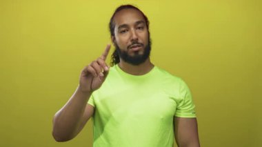 Adam sarı stüdyo ortamında kameraya bakarken işaret parmağı ile yukarı doğru işaret eder; özgüven odaklaması.