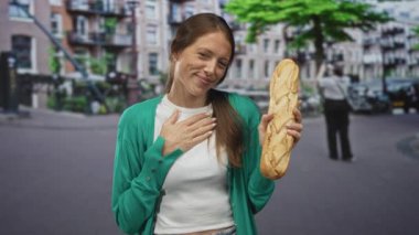 Kentin caddesinde elinde baget tutan yeşil hırka giyen ve gülümseyen bir kadın..