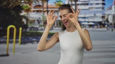 Caddelerde, binaların ve palmiye ağaçlarının yanında, göz kırpan ve gülümseyen bir kadın..