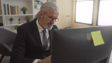 Ofis masasında elleri yanağında ve diş ağrısı çeken kırmızı gözlüklü, gri saçlı iş stresi olan takım elbiseli bir adam..