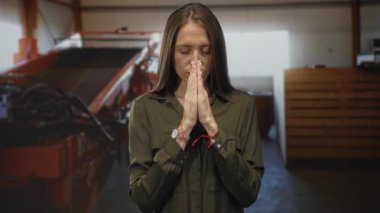 Elleri bir yapı atölyesinde dua etmek için birbirine bastırılmış bir kadın, gözleri kapalı ve parmakları birbirine dokunmuş; dinginlik.