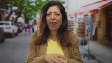 Orta yaşlı kadın kaşlarını çatıyor ve hatıra tezgahlarının yanındaki işlek cadde pazarında çenesini sıkıyor. Üzüntü..