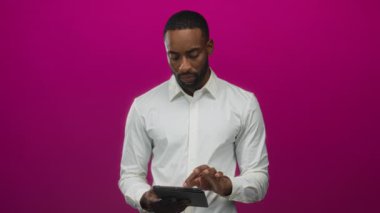 Genç Afro-Amerikalı bir adam yumuşak ışık altında eflatun stüdyoda çıplak elleriyle tableti tıklatıyor; verimlilik konsantrasyonu.