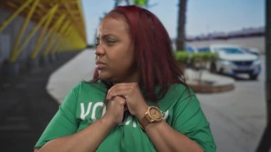 Gergin elleri olan ve sokakta yan yan bakan yeşil gönüllü gömlekli bir kadın..