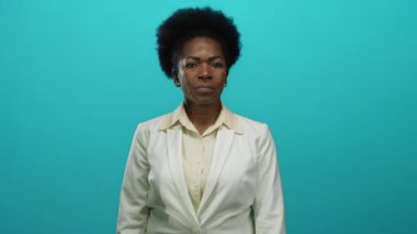 İzole edilmiş mavi arka planda beyaz takım elbise giyen, güçlü bir kadın..