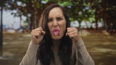 Genç İspanyol kadın, yeşil bir parkta gözlerini sıkarak bir jest yapıyor. Üzüntü, keder, hüsran, çaresizlik..