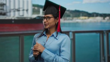 Bir yolcu gemisinin güvertesinde duran, açık hava manzaralı bir kep ve cübbe giyen Latin bir kadın..