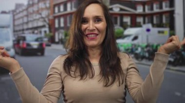 Genç kadın, her iki işaret parmağı da, park halindeki araçlar ve tuğla binalarla dolu işlek şehir caddesinde iki zıt yönü işaret ediyor; kararsızlık tercihi.