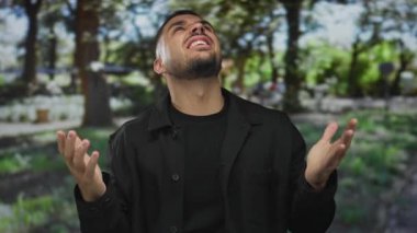 Genç İspanyol adam iki eliyle kulaklarını kapatır güneşli ormanda uzun yeşil ağaçların altında temizlenir; stres.