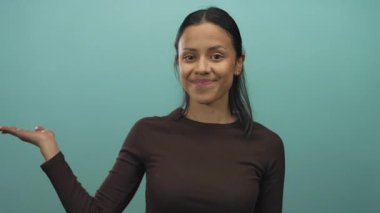 Gülümseyen İspanyol kadın avucunu yeşil bir zemine doğru gösteriyor, dostça bir hareketle kendine güveni ve cazibesi yayıyor..