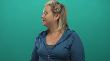 Mavi ceketli bir kadın yeşil bir stüdyoda parlak bir gülümsemeyle baş parmak işareti yapıyor..