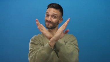 Yeşil kazaklı genç bir adam, mavi bir arka plana karşı x jesti ile ellerini çapraz yapar. Bu da kendine güvenen bir ifadeyle reddedildiğini gösterir..