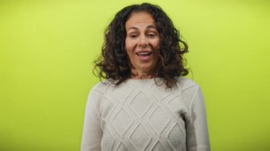 Kıvırcık saçlı bir kadın, canlı sarı bir duvarın karşısında mutsuzluktan mutluluğa dönüşüyor. Duygularını tek bir çerçevede gösteriyor..