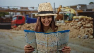 İnşaat alanında harita kullanan genç bir kadın, şehir arkaplanı içinde keşif ve macera öneriyor