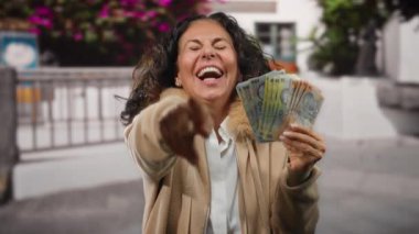 Şehrin dışındaki bir kadın, elinde neşeyle Romen banknotları ve kahkahalarla şehir ortamında saf mutluluk ve finansal başarıyı yakalıyor..