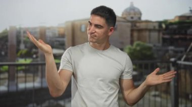 Avuç içleri havada ve omuz silkmiş genç İspanyol bir adam Roma 'nın harabelerinde açık bir terasta poz veriyor..