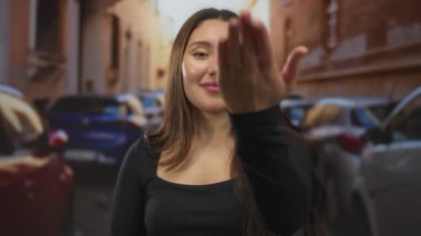 Kadın, güneşli şehir caddesinde, izleyiciye sıcak bir şekilde gülümseyerek jest yaparken elini uzatır; davet güven.