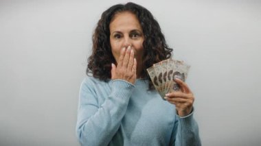 Orta yaşlı bir kadın Meksika pesolarını elinde tutuyor. Şaşırmış bir ifadeyle, düz beyaz bir duvara yaslanmış, mali başarıyı veya talih kuşunu tasvir ediyor..